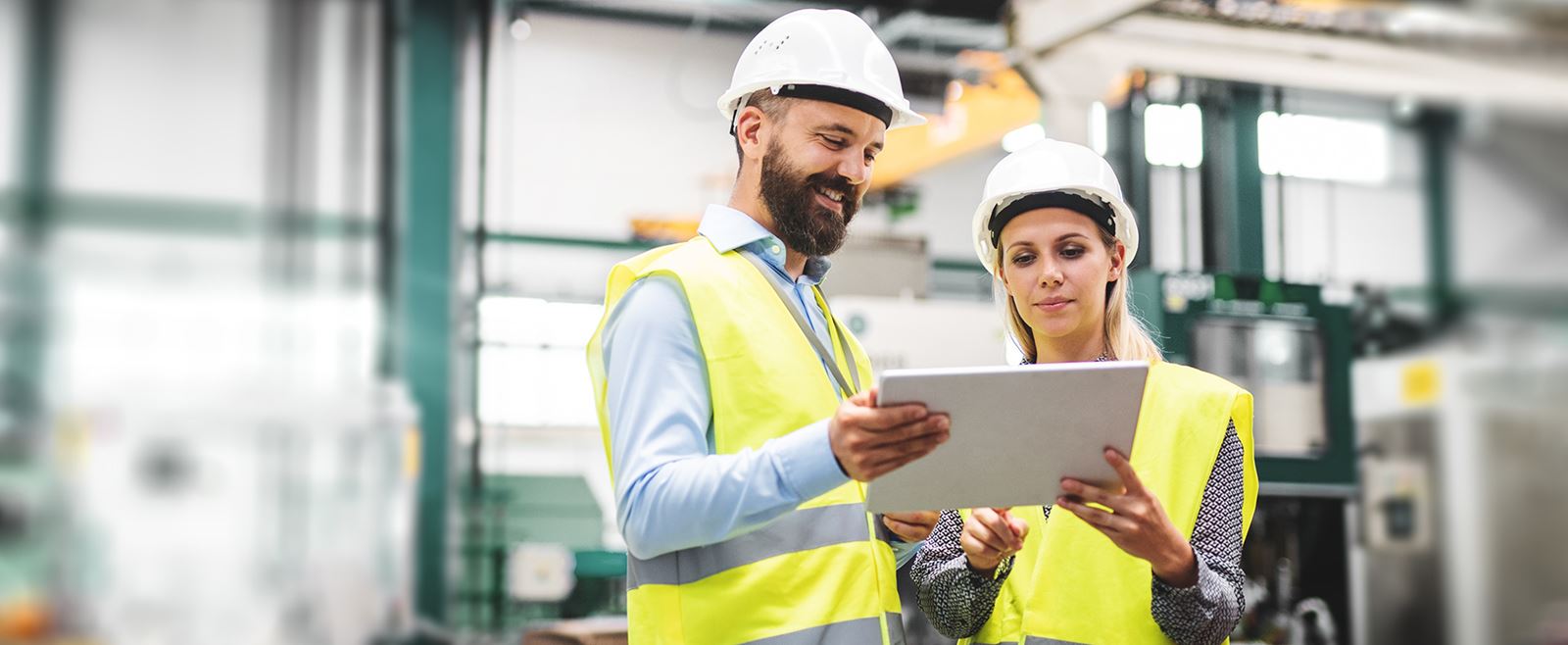 En man och kvinna i varselkläder i en fabrik, tittar på en skärm