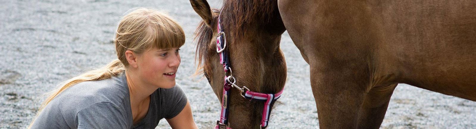 Flicka sitter på huk framför en häst som sänker sitt huvud mot henne