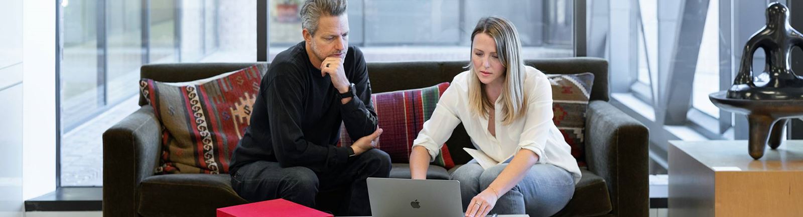 Man och kvinna sitter i en soffa framför en datorskärm och ser fundersamma ut