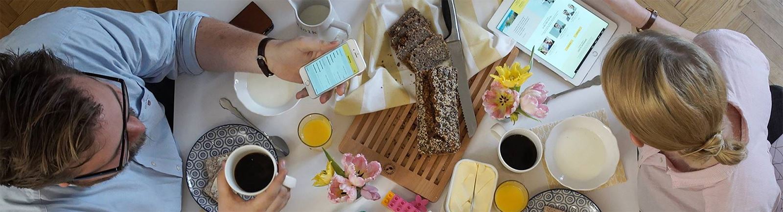 Par sitter vid frukostbordet med mobil och läsplatta. Fotograferade ovanifrån