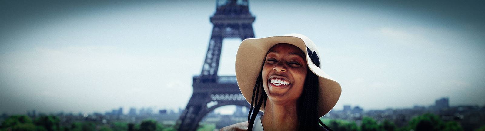 Glad kvinna med sommarhatt framför eiffeltornet i Paris