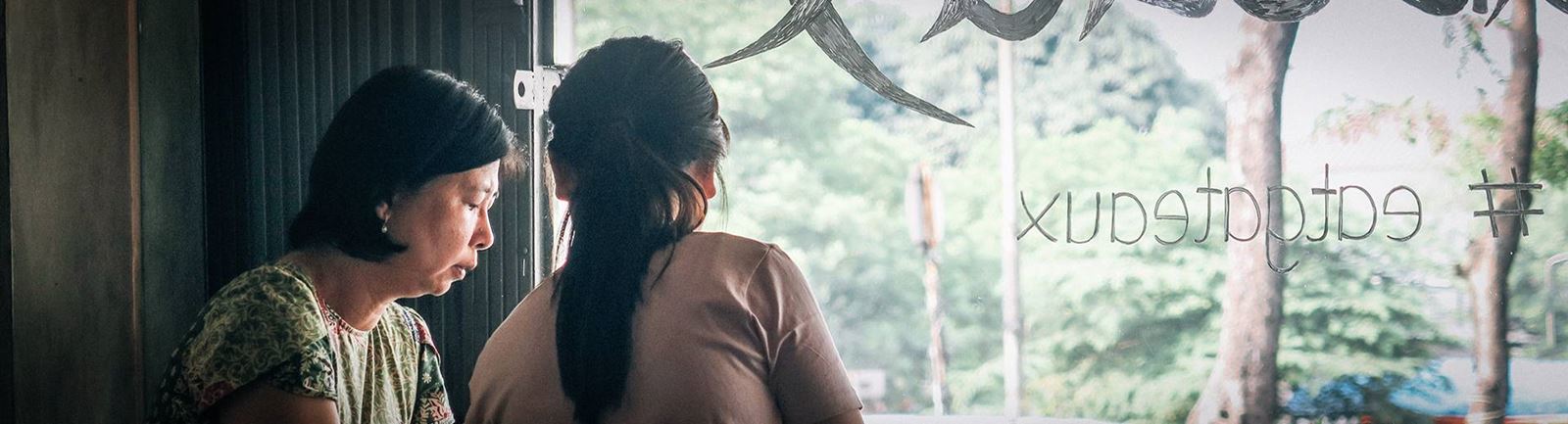 Två asiatiska kvinnor sitter i fönstret på ett café