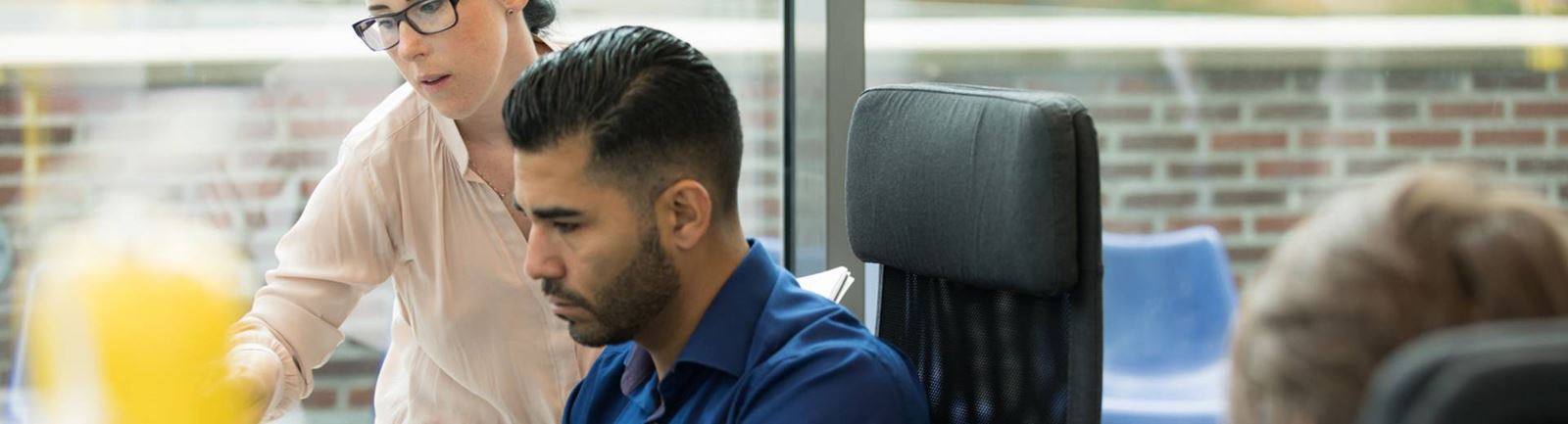 Man på kontor sitter framför datorn och en kvinnlig kollega står sidan om 