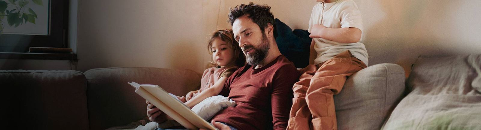 Pappa sitter i soffan och läser bok för två små barn
