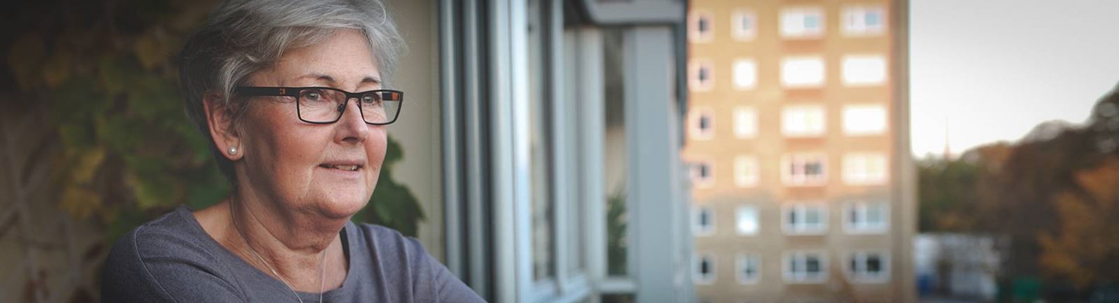 Mogen kvinna tittar ut från sin balkong på höghusområde
